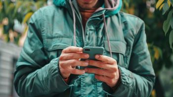 A man in a green jacket looking at a mobile phone