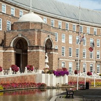 Exterior view of Bristol City Hall, a large brick civic building with an arched entrance, flower displays, and a water feature in the foreground on a bright day.