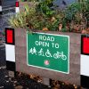 Close up photograph of green sign on a planter which says Road open to