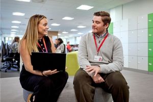 Two people sit talking together in an office environment