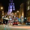 Photo of Park Street in Bristol at night, taken from the bottom of the hill with the Wills Memorial building lit up at the top of the hill and two people walking together to the left and cars driving up Park Street