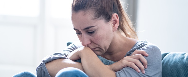 A lady sat on the floor with her arms crossed and head resting on her arms, looking sad.