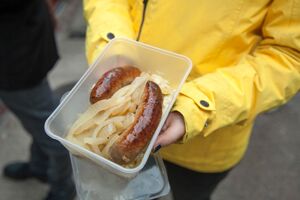 Someone holding a plastic container with sausage and onions in it